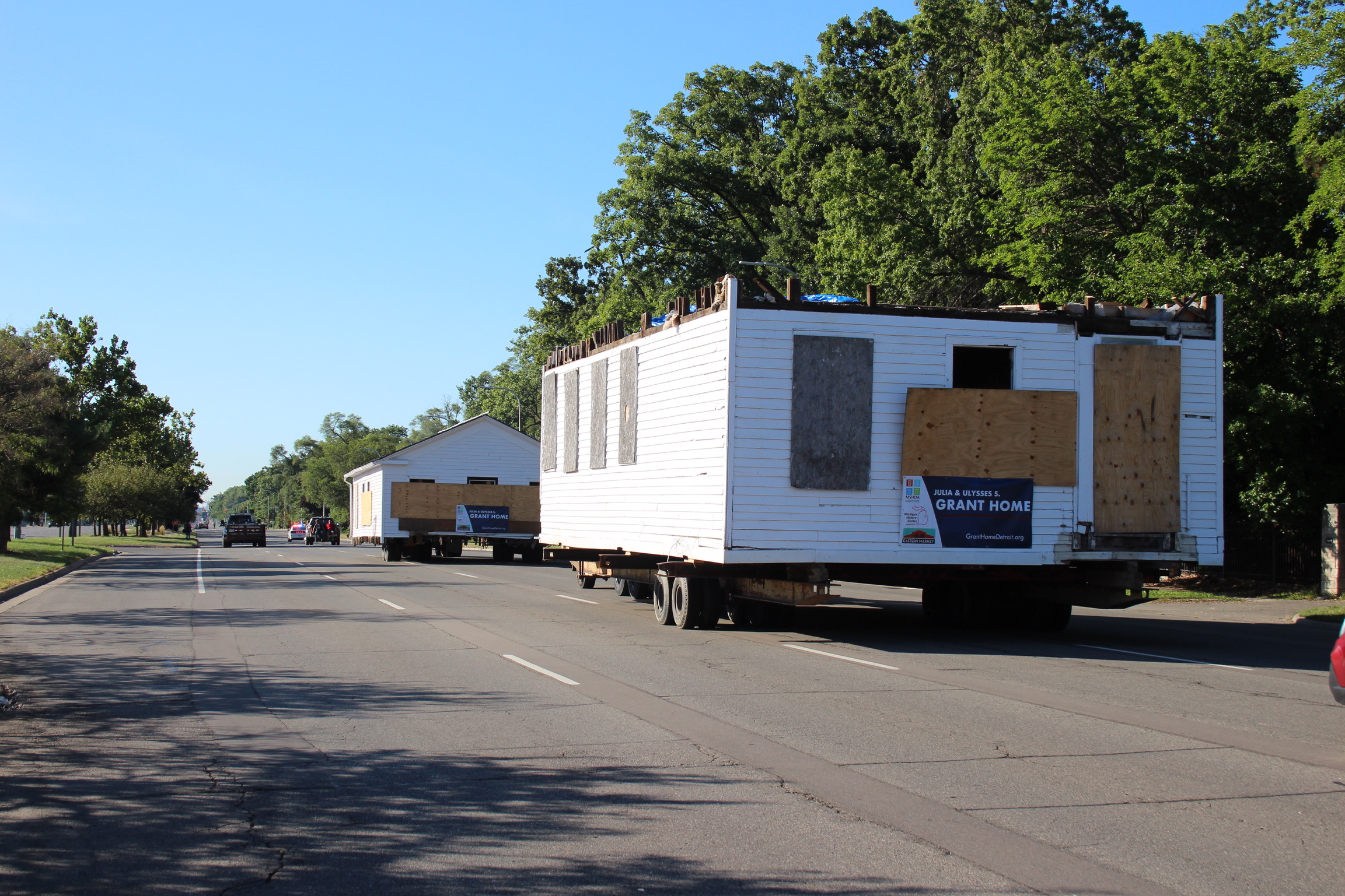 Two pieces of a home ride on trailers down a 5-lane road.